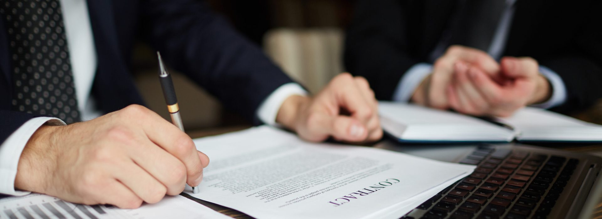 Closeup portrait of unrecognizable successful businessman wearing black formal suit reviewing documents and signing contract during meeting